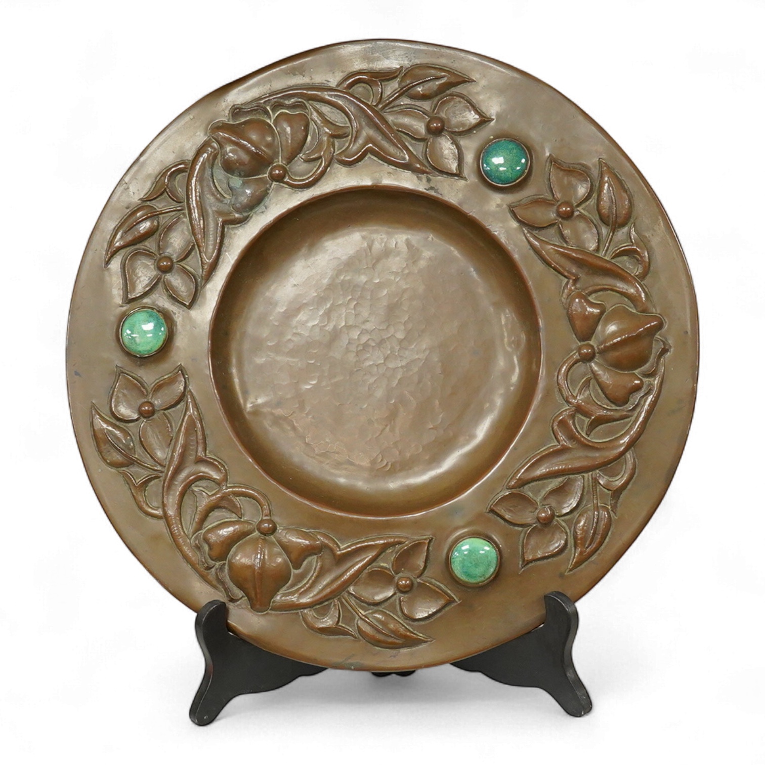 An Arts and Crafts embossed floral dish, in the manner of John Pearson, inlaid with Ruskin cabochons, unsigned, 32cm in diameter